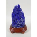 A large Chinese lapis lazuli carving of a mountain side village, on a wood stand, 22cm high