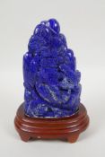 A large Chinese lapis lazuli carving of a mountain side village, on a wood stand, 22cm high