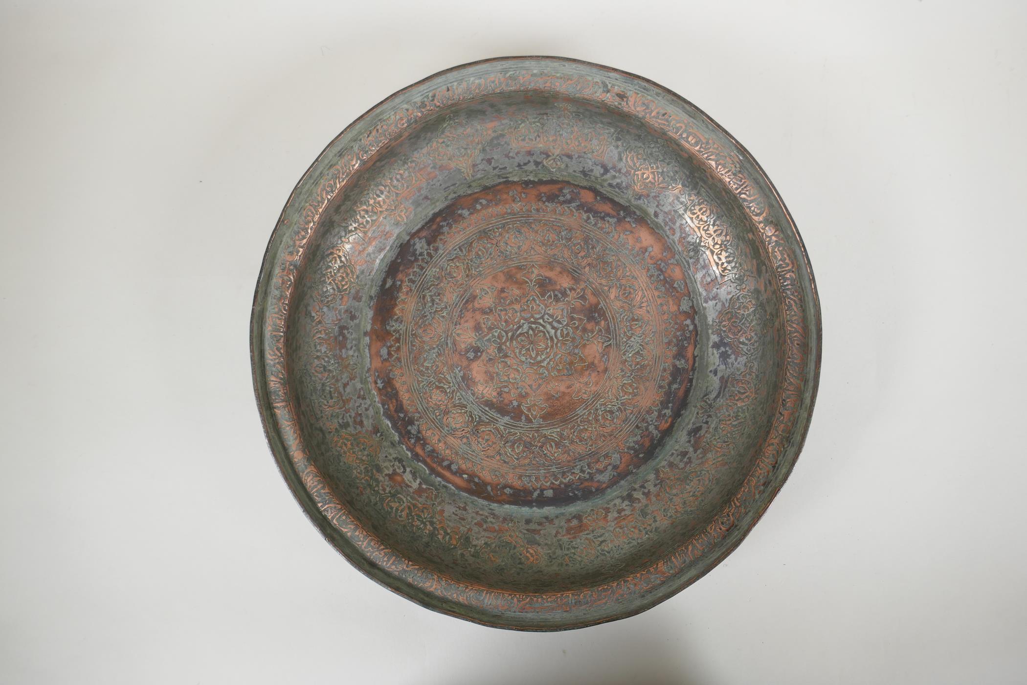 An antique Islamic copper dish with chased script and floral decoration, 34cm diameter