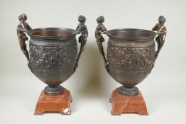 A pair of Grand Tour style bronze urns on red marbled bases, with male figural twin handles, 41cm