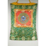 A Tibetan hand painted Mandala, in an embroidered silk mount, 53 x 67cm