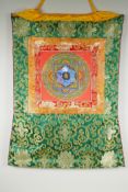 A Tibetan hand painted Mandala, in an embroidered silk mount, 53 x 67cm