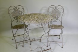 A painted and distressed metal bistro table and two folding chairs, 69cm diameter