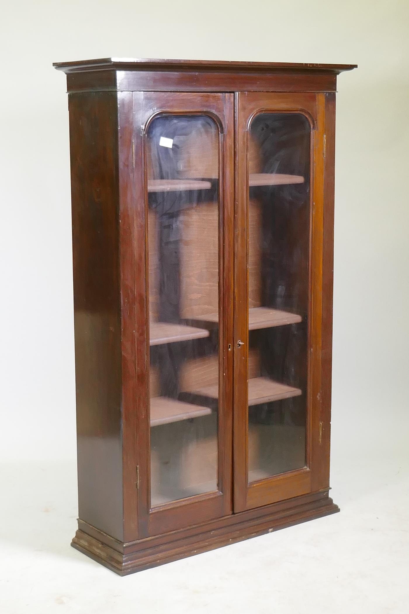 A Victorian mahogany bookcase with two arched glazed doors, raised on a shaped plinth, 86 x 30 x