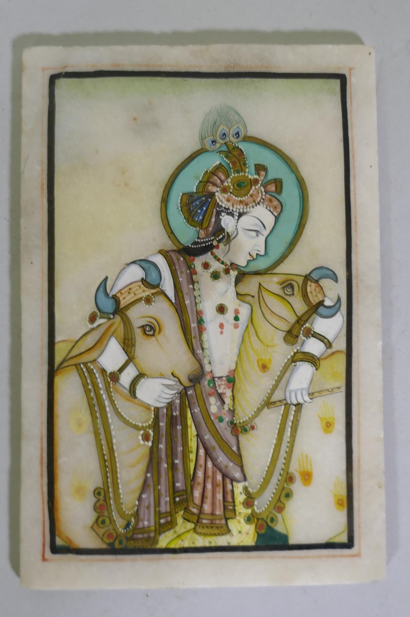 An Indian painting of Krishna, bearing a flute and accompanied by two cows, enamels on marble