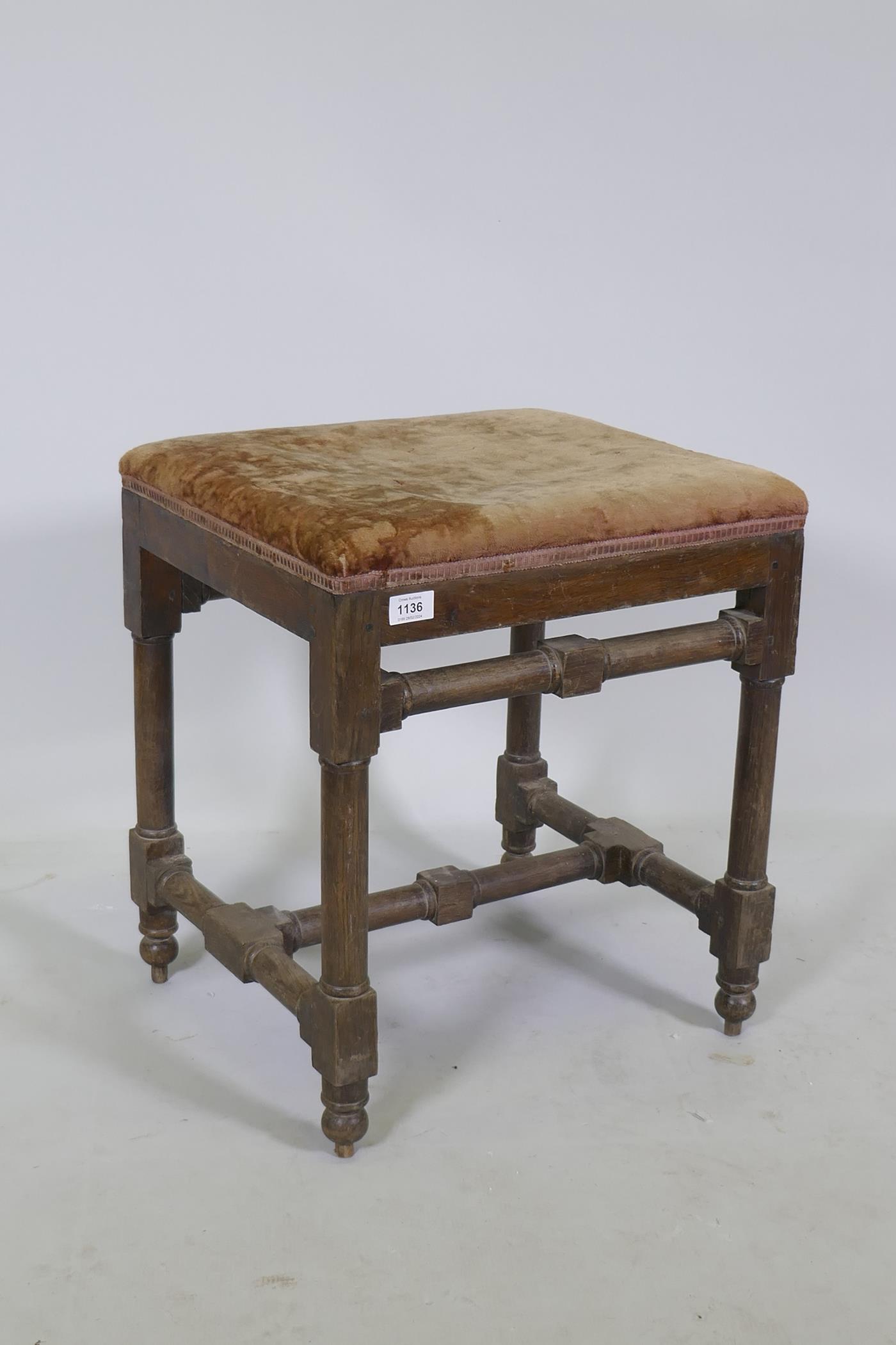 A good quality antique oak stool, raised on turned supports united by stretchers and pegged
