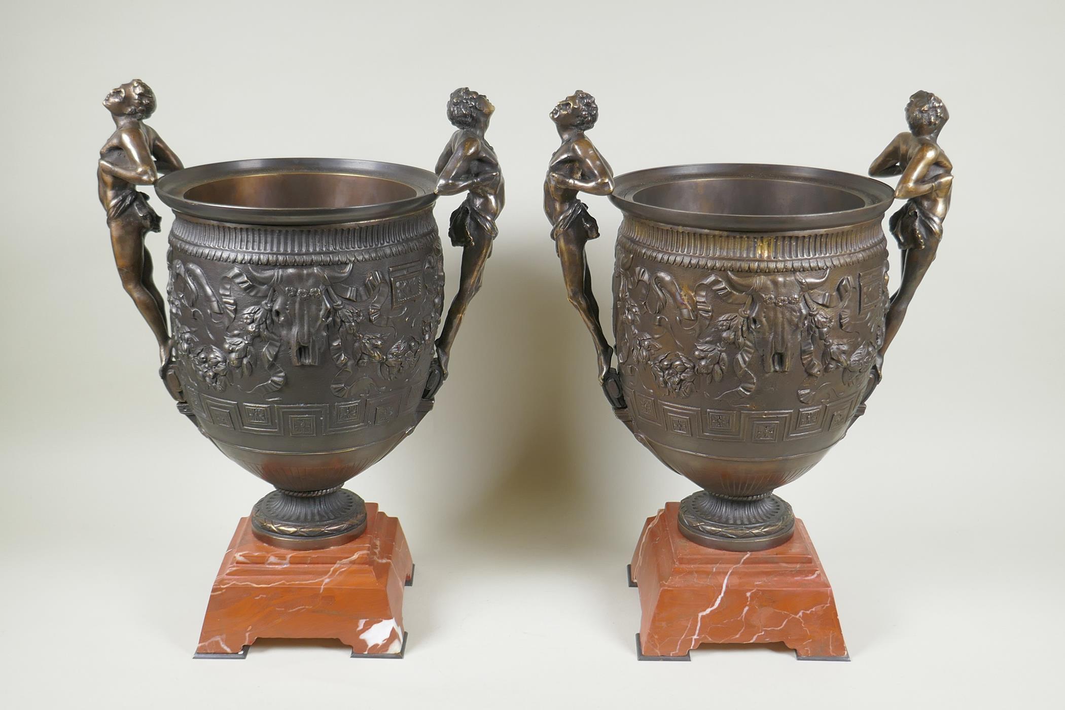 A pair of Grand Tour style bronze urns on red marbled bases, with male figural twin handles, 41cm