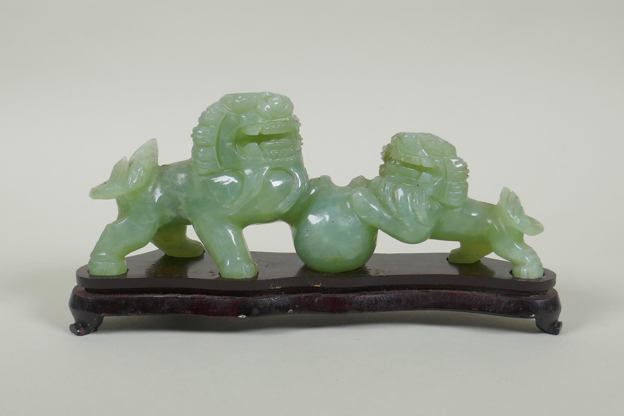 A Chinese celadon jade carving of twin fo-dogs, on a lacquered wood stand, 21cm long