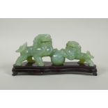 A Chinese celadon jade carving of twin fo-dogs, on a lacquered wood stand, 21cm long