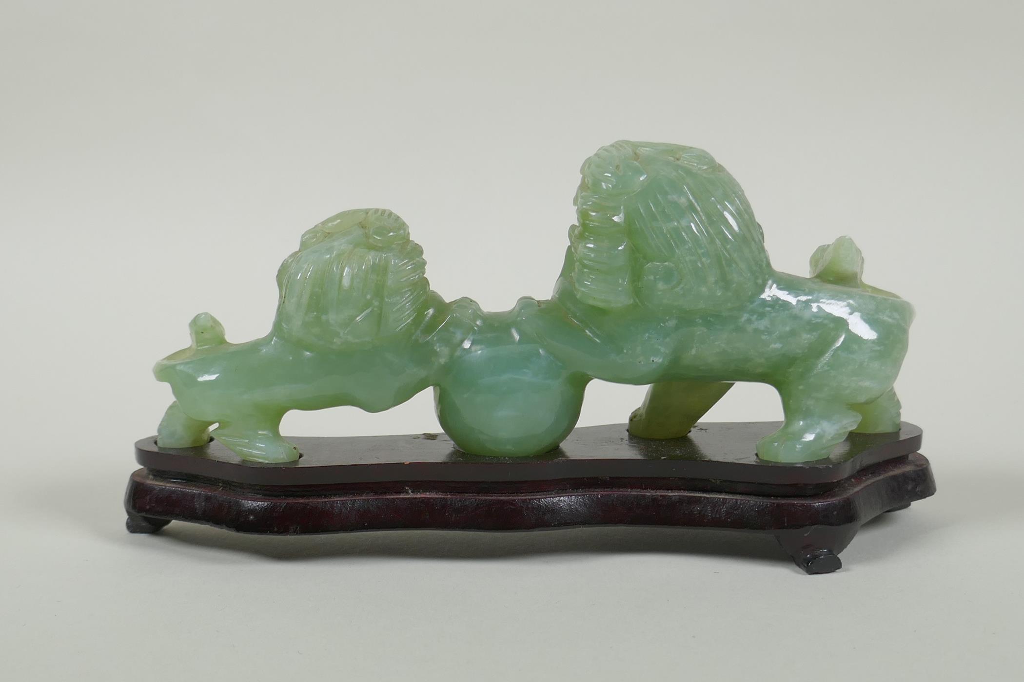 A Chinese celadon jade carving of twin fo-dogs, on a lacquered wood stand, 21cm long - Image 2 of 2