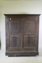 An early C18th two door cupboard with fielded panel doors and panelled sides, raised on a plinth