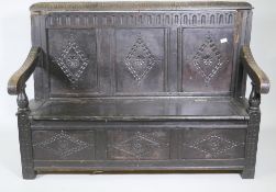 An C18th oak settle with carved panel back and front, lift up seat, raised on stile supports, with