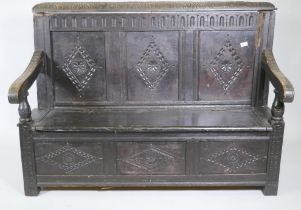 An C18th oak settle with carved panel back and front, lift up seat, raised on stile supports, with