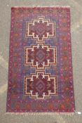 A Persian Baluch red and blue wool rug decorated with two geometric medallions, 104 x 180cm