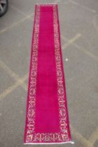 A large five hand woven Persian runner with a plain pink field and decorative border, 390 x 75cm