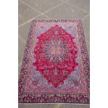 A claret and blue ground Persian Mashad carpet with a traditional floral medallion design,