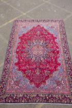 A claret and blue ground Persian Mashad carpet with a traditional floral medallion design,