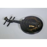 A wood wall ornament with raised decoration, in the form of an Oriental stringed musical instrument,