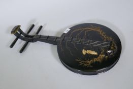 A wood wall ornament with raised decoration, in the form of an Oriental stringed musical instrument,