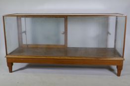 An oak framed glass shop cabinet with two sliding doors, raised on turned supports, 178  x 58 x 93cm
