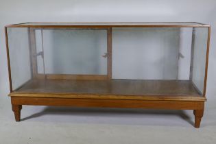 An oak framed glass shop cabinet with two sliding doors, raised on turned supports, 178  x 58 x 93cm