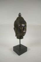 A gilt composition Buddha head on a display stand, 35cm high