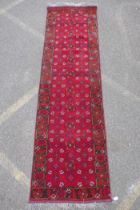 A rich red ground Persian wool runner with an allover geometric design and black borders, 84 x 290cm