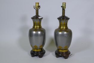 A pair of white metal table lamps with brass Oriental style lotus leaf decoration, on wood bases,