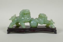 A Chinese celadon jade carving of two fo-dogs, on a lacquered wood stand, 21cm long