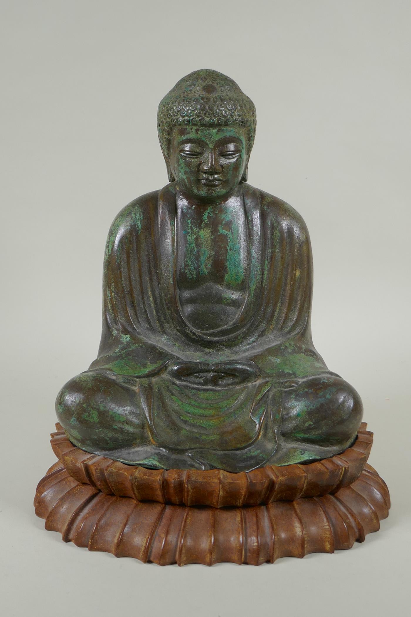 A Chinese patinated bronze figure of Buddha seated in meditation, on a carved hardwood stand, 31cm