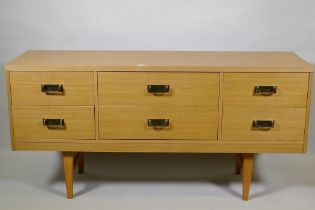 A mid century faded sapele six drawer chest with brass handles, raised on square tapering