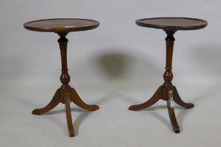 A pair of solid yew wood wine tables with dished tops, raised on turned columns with splay supports,