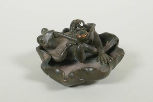 A bronze figure of a smoking frog reclining on a lily pad, 8cm diameter