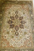 An Oriental silk carpet with floral designs and central medallion on a cream and faded terracotta