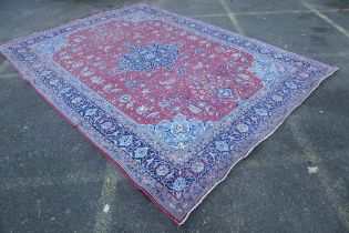 A large Persian red ground wool carpet with floral medallion design and blue borders, some wear,