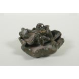 A bronze figure of a smoking frog reclining on a lily pad, 8cm diameter