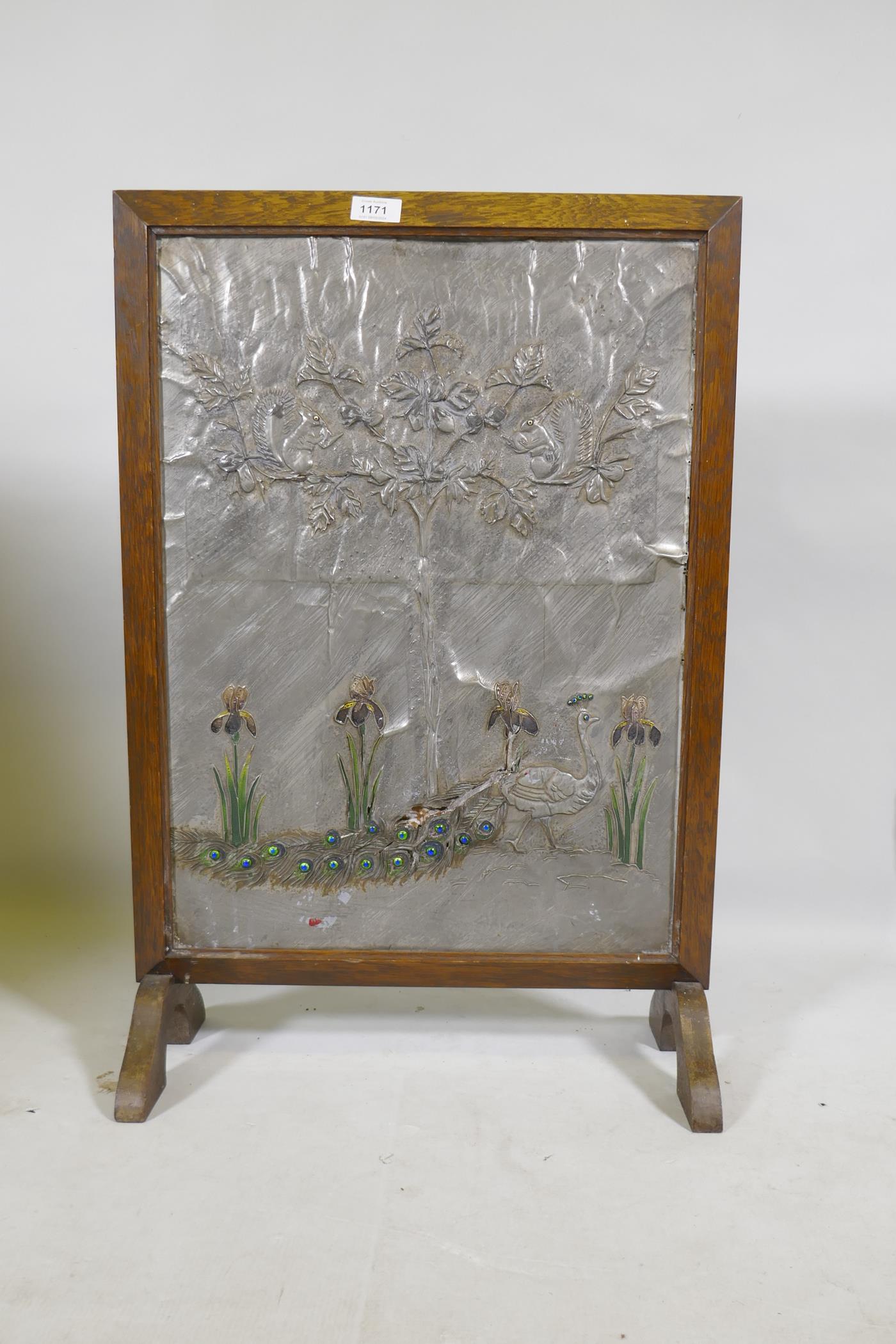 An Arts & Crafts firescreen with inset pewter and enamel panel, decorated in repousse with a peacock