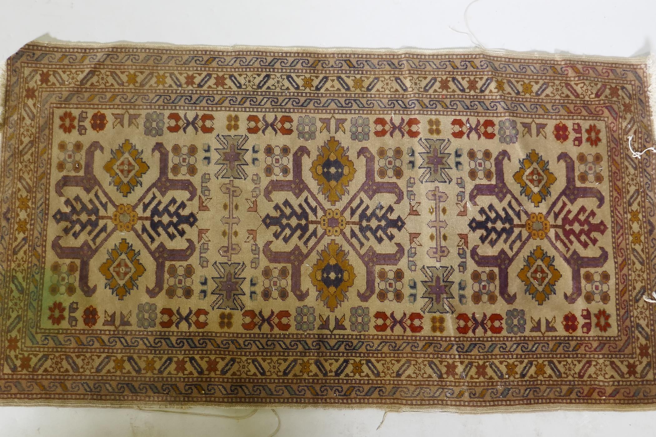 An antique hand woven Oriental rug with geometric designs n a buff coloured field, 68 x 125cm