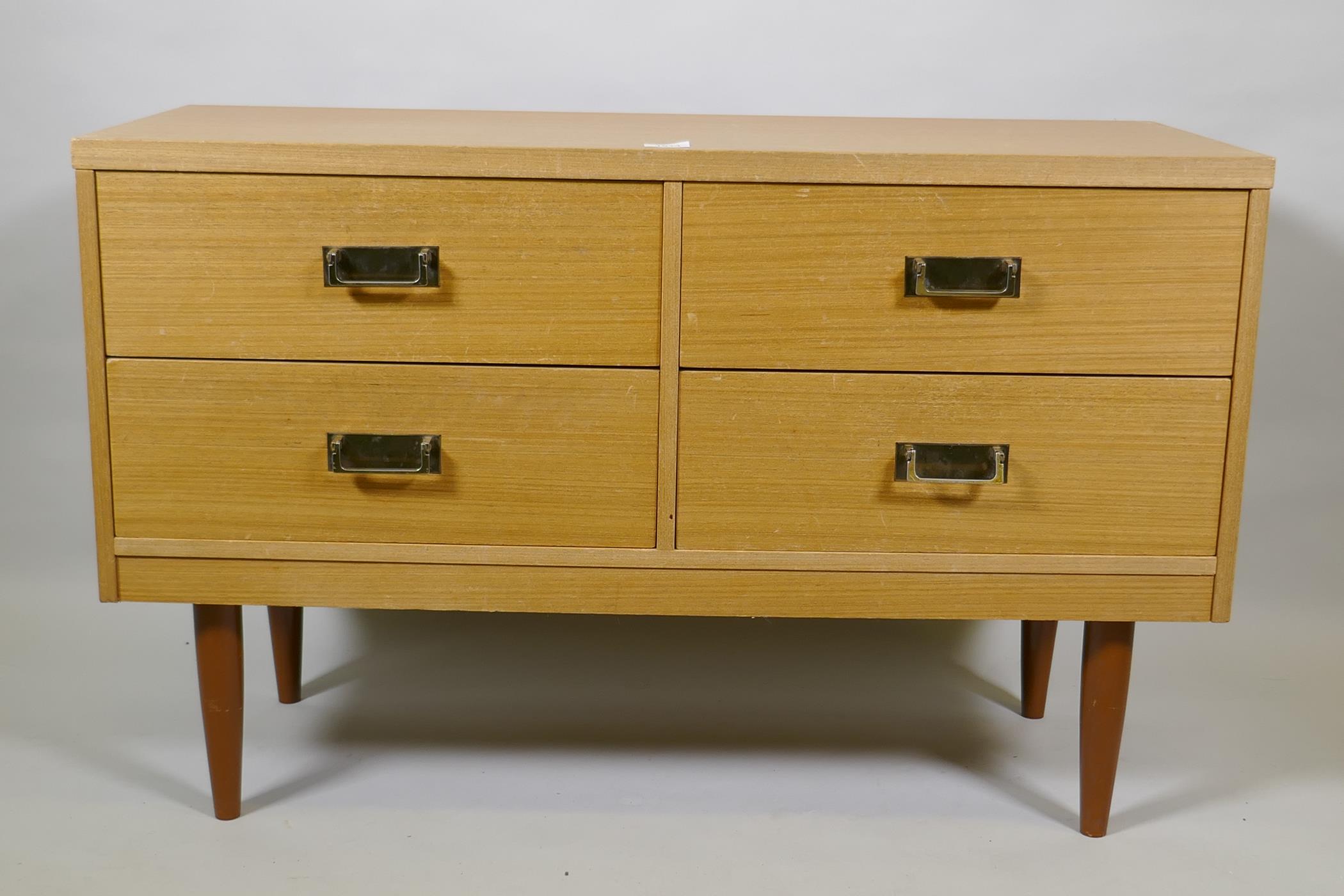A mid century faded sapele four drawer chest with brass handles, raised on tapering supports, 101