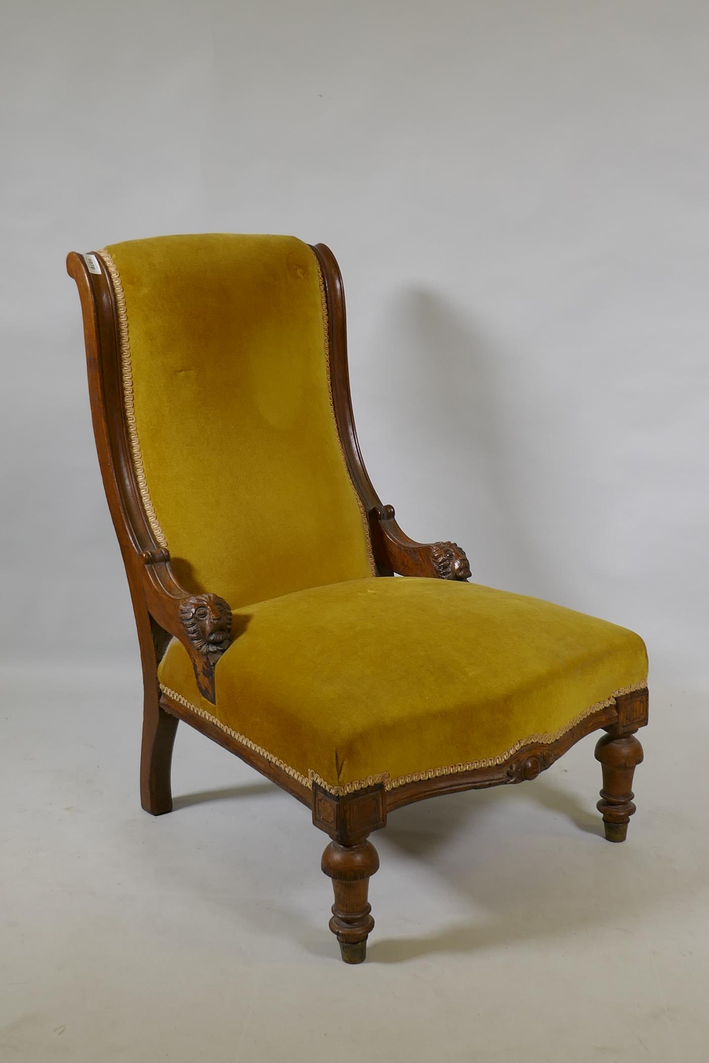 A C19th oak nursing chair with carved lion mask decoration, raised on turned supports