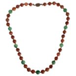 A Chinese green and russet jade bead necklace with silver filigree clasp.