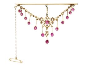 An Edwardian ruby and seed pearl set high purity gold scroll pendant, later applied to a brooch.