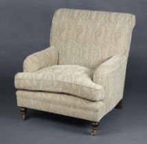 A Howard style armchair upholstered in light coloured paisley style material, raised on turned