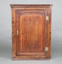 A Georgian oak corner cabinet with moulded and dentil cornice, fitted shelves enclosed by a panelled