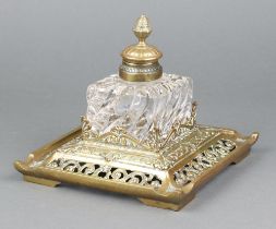 A Victorian square cut glass inkwell with hinged lid, raised on a pierced brass base marked CS