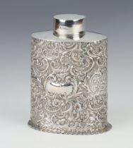 A Victorian oval repousse silver tea caddy decorated with scrolls and flowers and vacant
