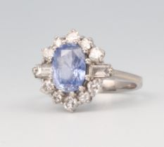 A white metal oval cornflower sapphire and baguette and brilliant cut diamond cluster ring, the