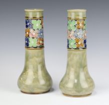 A pair of Royal Doulton green salt glazed vases decorated with a band of stylised floral heads,