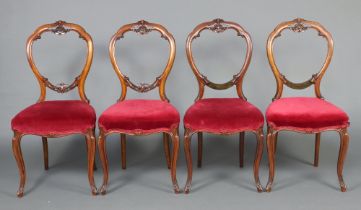 A set of 4 Victorian carved walnut balloon back dining chairs with over stuffed seats, raised on