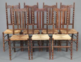 A set of 7 Art Nouveau oak stick and rail back dining chairs with woven rush seats, raised on bobbin